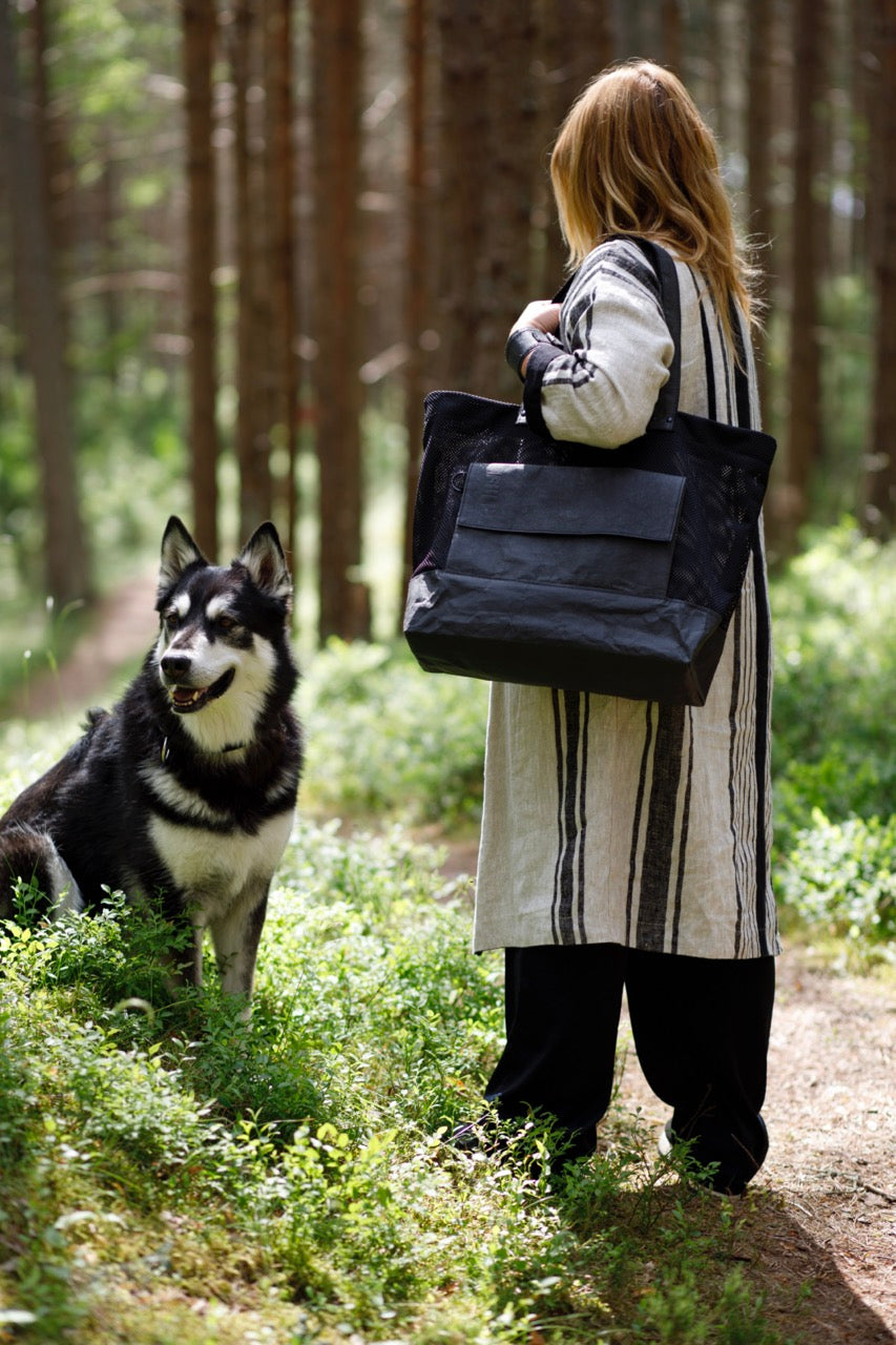 Black Fiilii design kraftex paper bag on womans shoulder in forest with dog nex to her. 