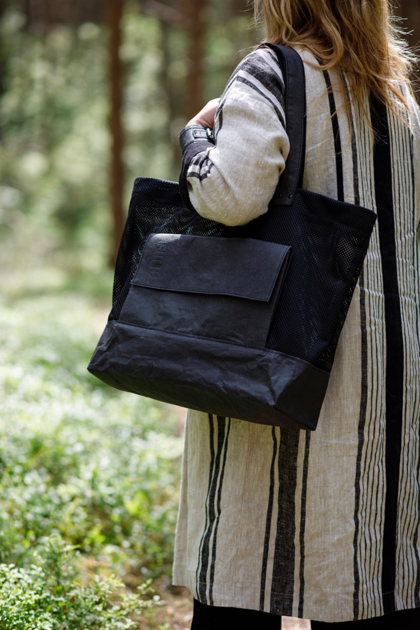 Black kraft paper fabric bag on womans shoulder in forest.