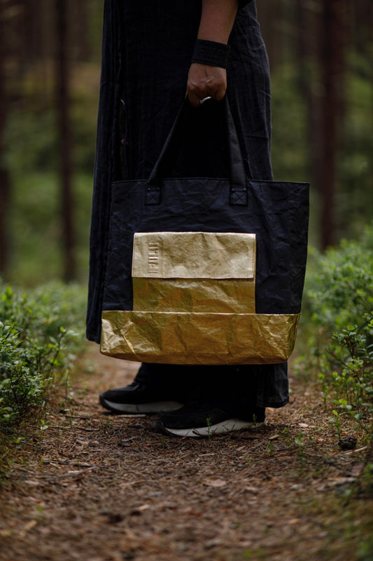 Golden black Fiilii design bag in persons hands, in forest.