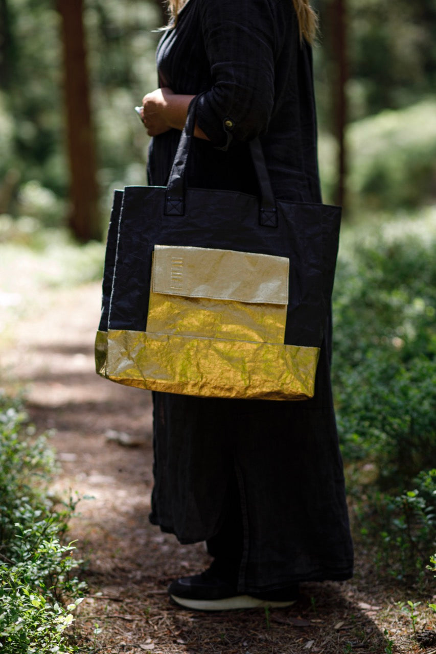 Golden black Fiilii design bag in persons hands in forest. 