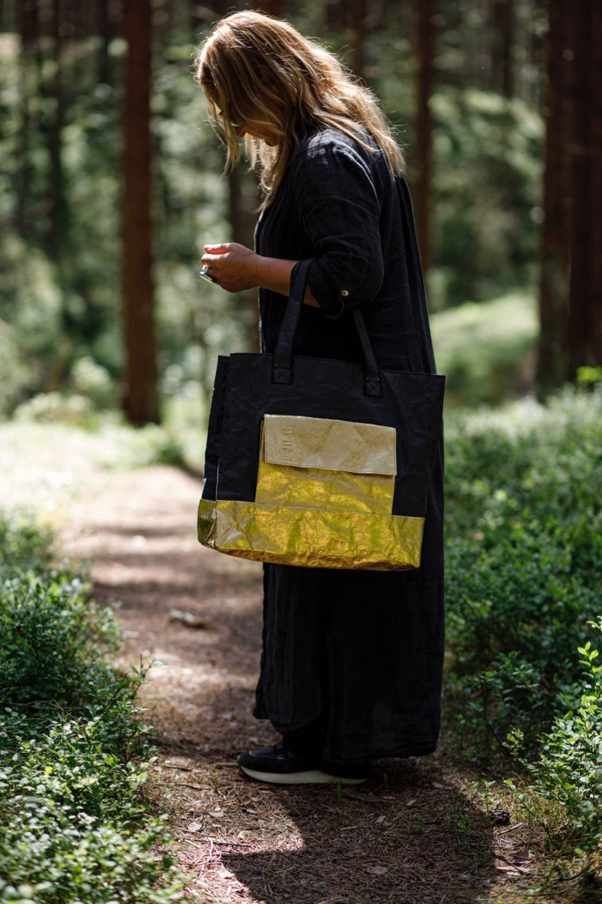 Woman holding golden black Fiilii design bag in forest. 